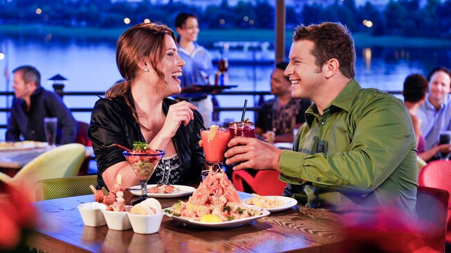 A woman and man share a laugh as they toast over their dinner