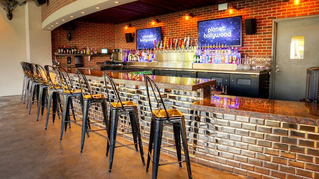 Stargazers Bar in Disney Springs featuring a granite topped bar, tall stools, brick accents and shelves of liquor bottles