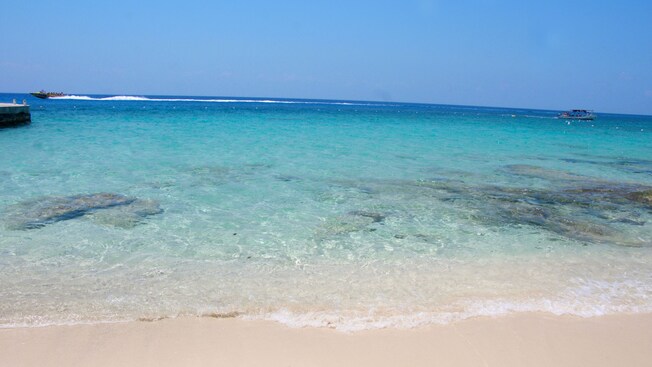 A sunny beach with 2 boats cruising across the water in the distance