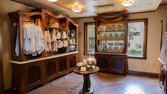 A section of Plume Et Palette shop in Epcot with wooden cabinets displaying shirts, bags and other Disney merchandise