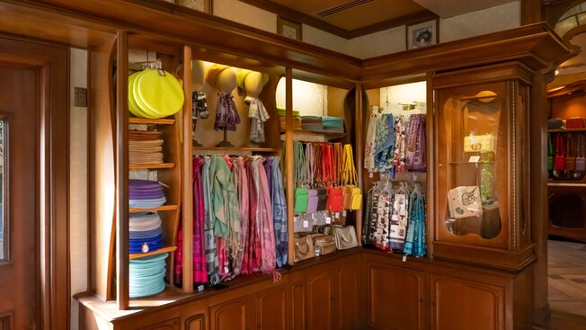 A wooden shelf and hanger displaying a variety of clothing and personal accessories in Plume Et Palette at Epcot