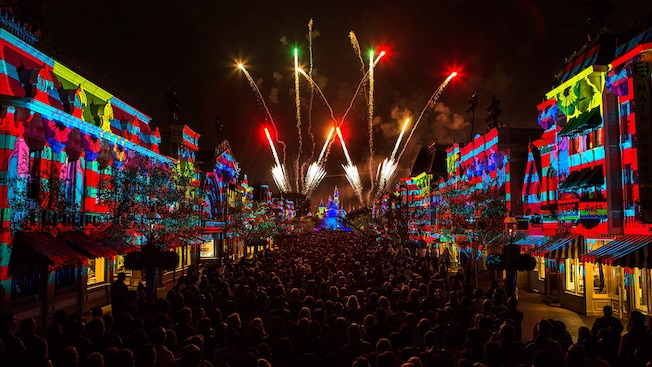 A crowd of people gather along Main Street U.S.A. as fireworks burst over Sleeping Beauty Castle