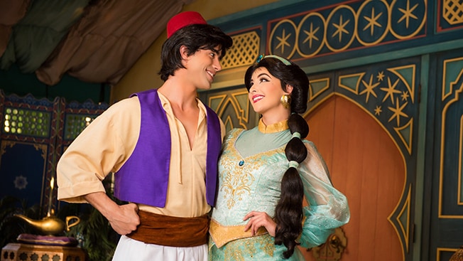 Aladdin and Disney Princess Jasmine stand arm in arm, smile and gaze into each others eyes

