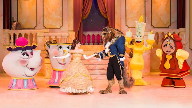 The Beast dances with Belle on stage while Lumiere, Cogsworth, Mrs. Potts and Chip look on in glee