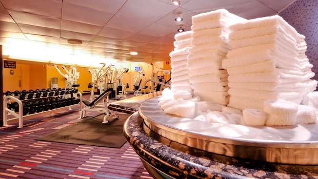 Stacks of towels in a gym with exercise equipment and barbells
