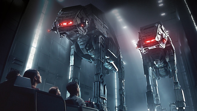 People in a transport vehicle inside a hanger bay look up at 2 towering AT-AT walkers