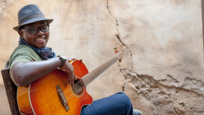 Nathi, from the Afropop band Wassalou, sits in a chair with a guitar 