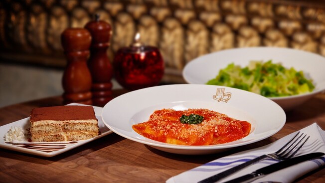Platos con ensalada, ravioli y tiramisú distribuidos sobre una mesa