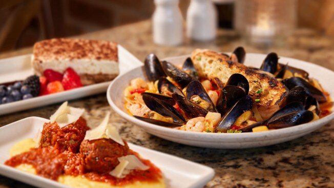 Un plato con albóndigas, un plato con fettuccini de mariscos y un plato con tiramisú