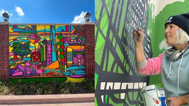 A mural featuring buildings from cities around the world. Mila Sketch holds a bucket of paint while working on a mural.