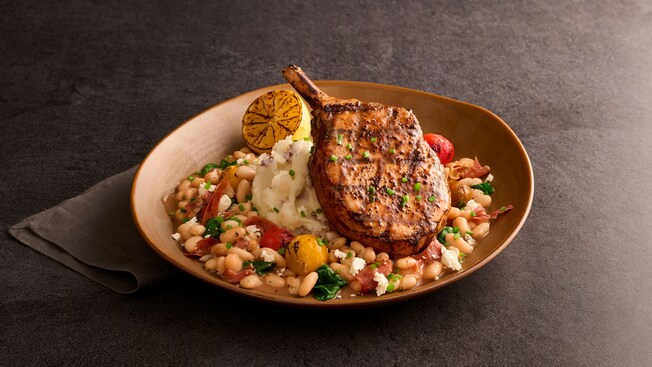 A pork chop over a white bean ragout with spinach, feta cheese and tomatoes, served with mashed potatoes