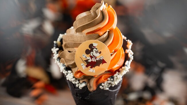 A Vampire Mickey Cone with pumpkin and chocolate soft serve swirl, topped with sprinkles and a chocolate Mickey Mouse coin