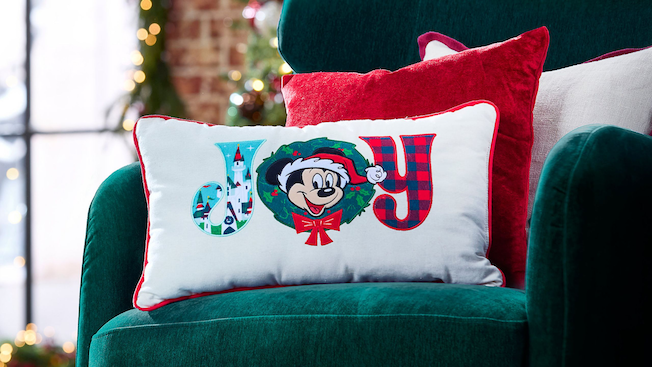 Un cojín decorativo con temática de Navidad en el que aparece Mickey Mouse y la palabra “Joy”