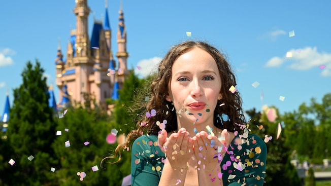 A woman blows confetti while standing near Cinderella Castle