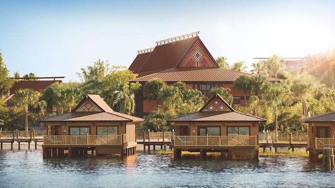 Three bungalows along the water with palm trees in the background