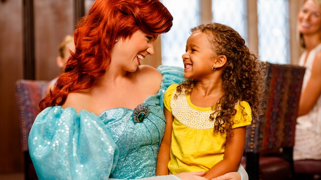 An ecstatic little girl sits on the lap of Princess Ariel at Cinderella's Royal Table