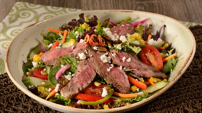 Salad with mixed greens, bell peppers, tomatoes, onions, cucumber, corn, pumpkin seeds, steak and cheese