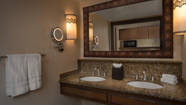 Um gabinete de banheiro com bancada de granito, 2 pias, um espelho emoldurado e 2 arandelas