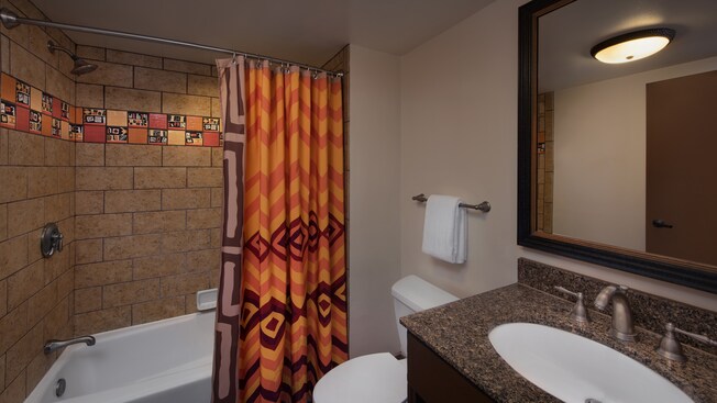 Um banheiro com chuveiro e banheira, cortina no box com tema africano e azulejo decorativo