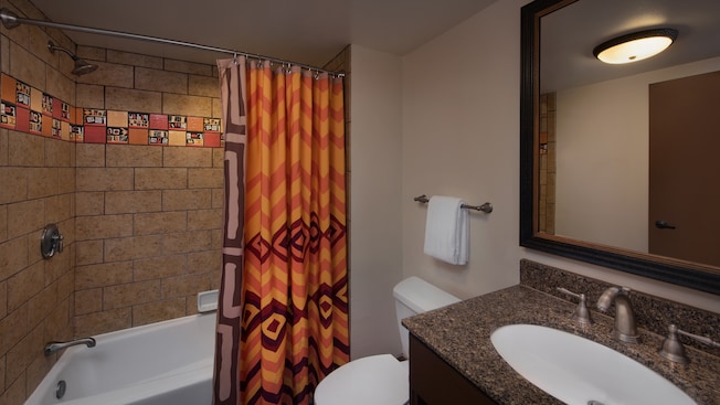 Um banheiro com chuveiro e banheira, cortina no box com tema africano e azulejo decorativo