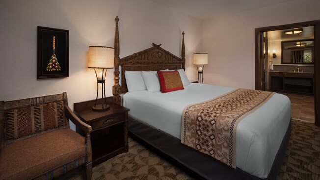 Um quarto com tema africano com uma cama, mesas de cabeceira com luminárias, cadeira e quadro