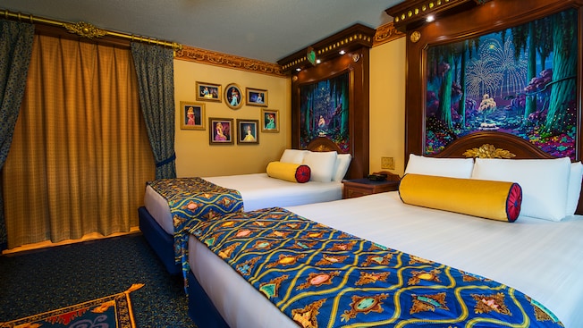 Royal bedroom with 2 beds, tall regal headboards, framed Disney princesses, gold-curtained bathroom