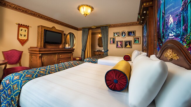 Royal-themed bedroom, 2 beds, elegant dresser with wood-framed TV, Disney princess art, brocade chair