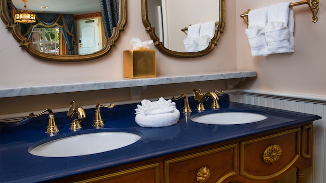 Royal 2-sink bathroom vanity with gold fixtures and mirrors, marble ledge, wainscoting, towels