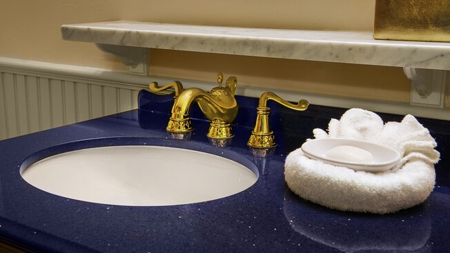 Royal gold bathroom sink fixtures and marble ledge with faucet shaped like Aladdin's lamp, hand towels