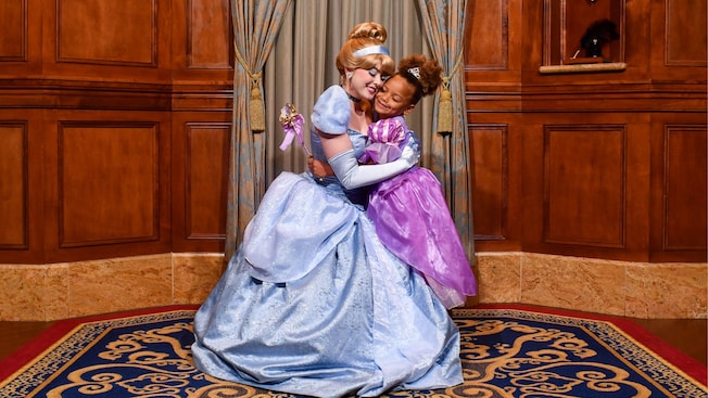 A young girl dressed like a princess hugs Cinderella