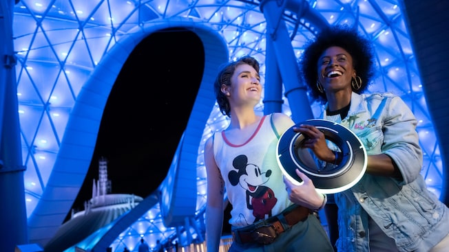 Two friends hold an Identity Disc in front of the TRON Lightcycle Run attraction at Walt Disney World Resort