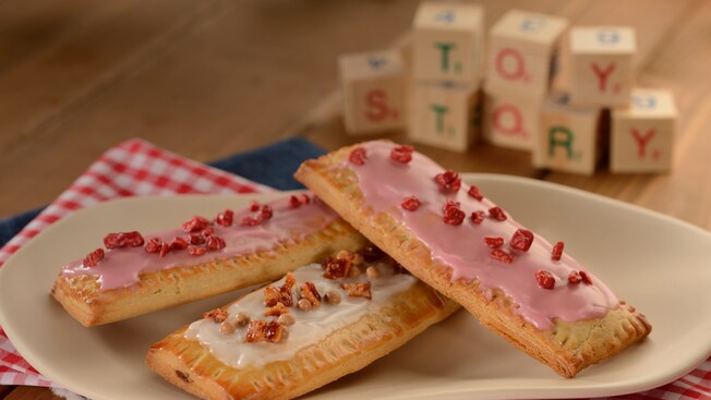 Pastries topped in frosting, bacon and candy resting on a plate and a tablecloth