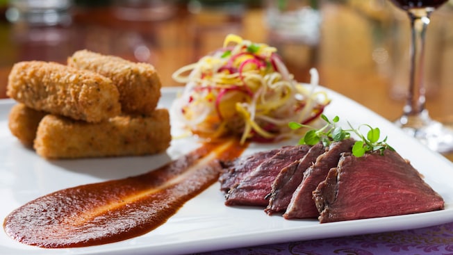 A plate of sliced beef with a side of croquettes