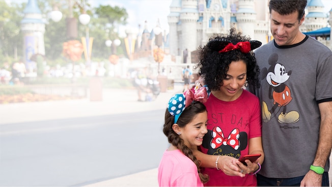A family looks at a cell phone near Cinderella Castle
