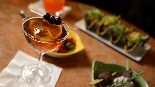 A spear with 3 olives rests across the rim of a specialty cocktail at Carthay Circle Lounge
