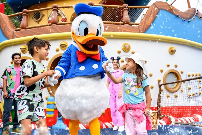 Donald Duck greeting children as bubbles float around a boat
