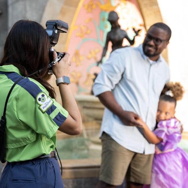 A Photo Pass Cast Member photographs a father and his daughter at Cinderella Castle