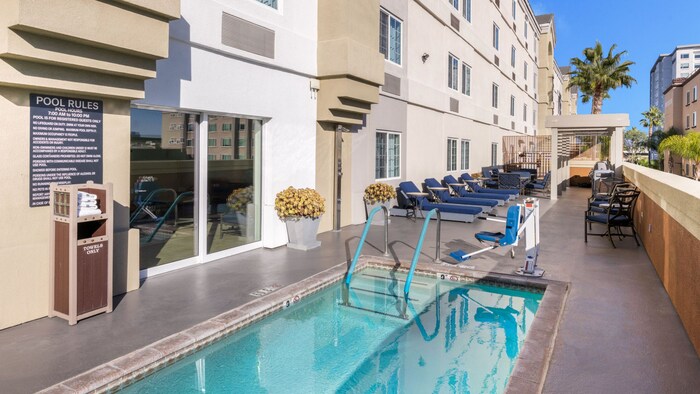 The outdoor pool and recreation area of Candlewood Suites Anaheim Resort Area featuring a lift for accessibility, loungers, tables and chairs