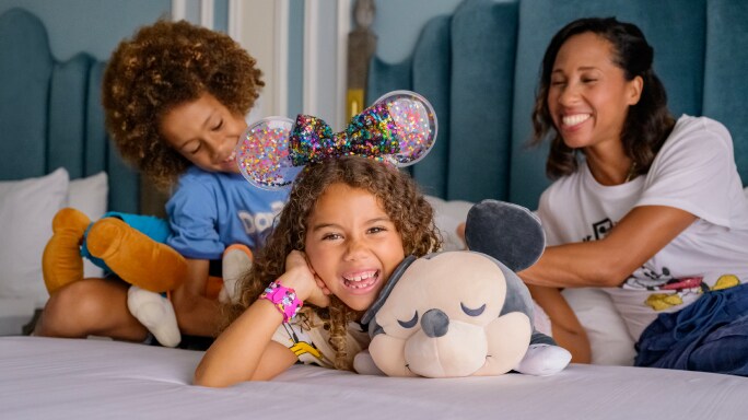 A mom and her two young daughters laughing on a bed