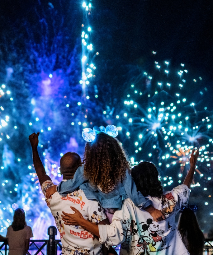 A mom and dad holding their daughter on their shoulders during a fireworks show