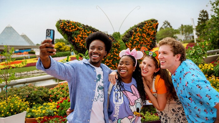 2 couples pose together for a selfie in front of a giant butterfly topiary