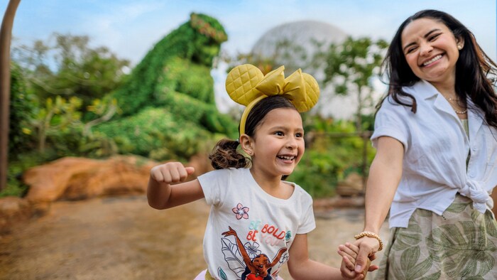 A girl wearing a Minnie Mouse ear headband holding hands with her mother in front of a topiary of Te Fiti
