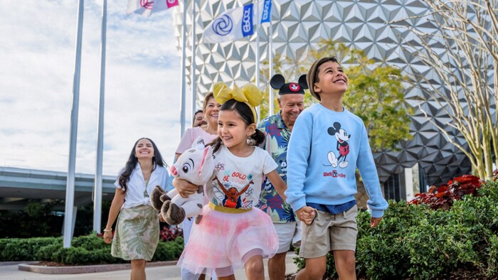 Uma família de 6 pessoas em pares, de mãos dadas, perto da Spaceship Earth no EPCOT
