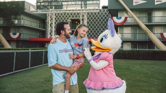 Un adulto sostiene a un niño mientras conocen a Daisy Duck