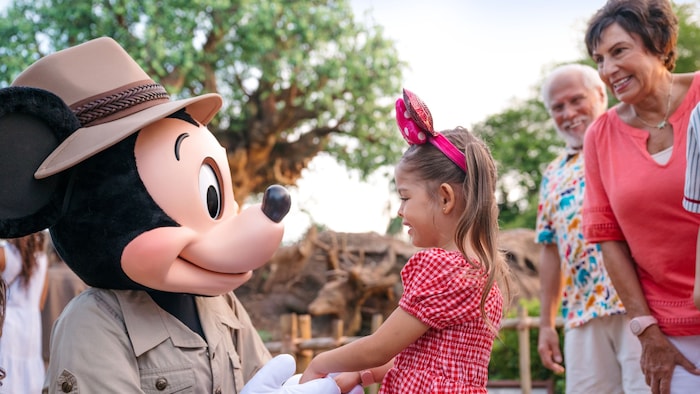 Mickey Mouse holding hands with a girl as her family stands nearby