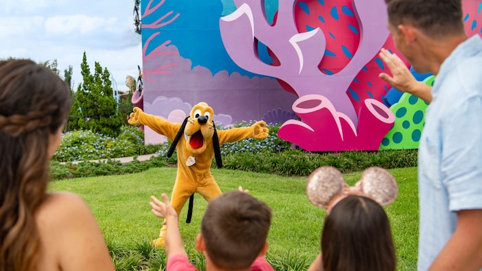 Pluto posing with his arms outstretched as 4 Guests stand nearby at Disney's Art of Animation Resort