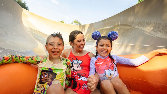 A mother and 2 young children riding in a raft on a water slide