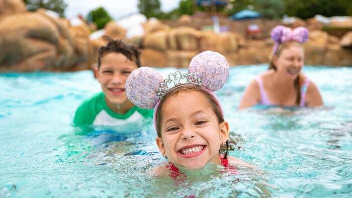 A mother and 2 young children swimming in a pool together at Disney’s Blizzard Beach water park  