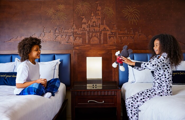 Three children wearing Disney themed bathrobes laughing on a bed in a Disneyland Resort hotel room