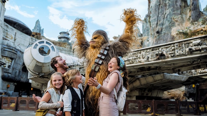 A family happily interacting with Chewbacca while standing near the Millennium Falcon Smugglers Run attraction.